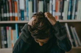 Estudiante agobiado con las manos en la cabeza ante una estantería de libros tras suspender la selec